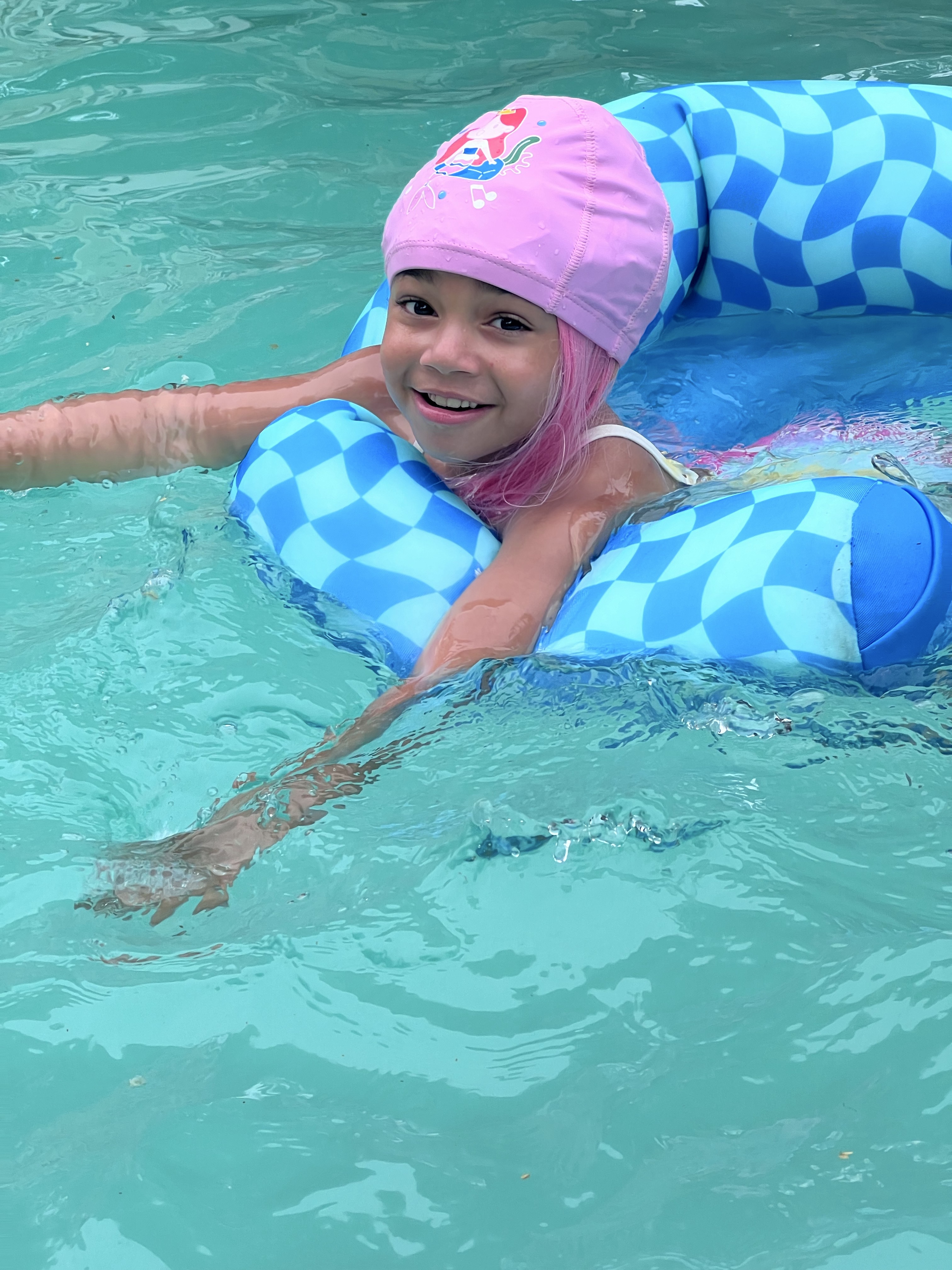 Child swimming through a pool with long pink play hair trailing behind them.